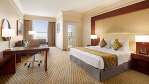 A hotel room with a large bed, a desk, a chair, and a view of the city.