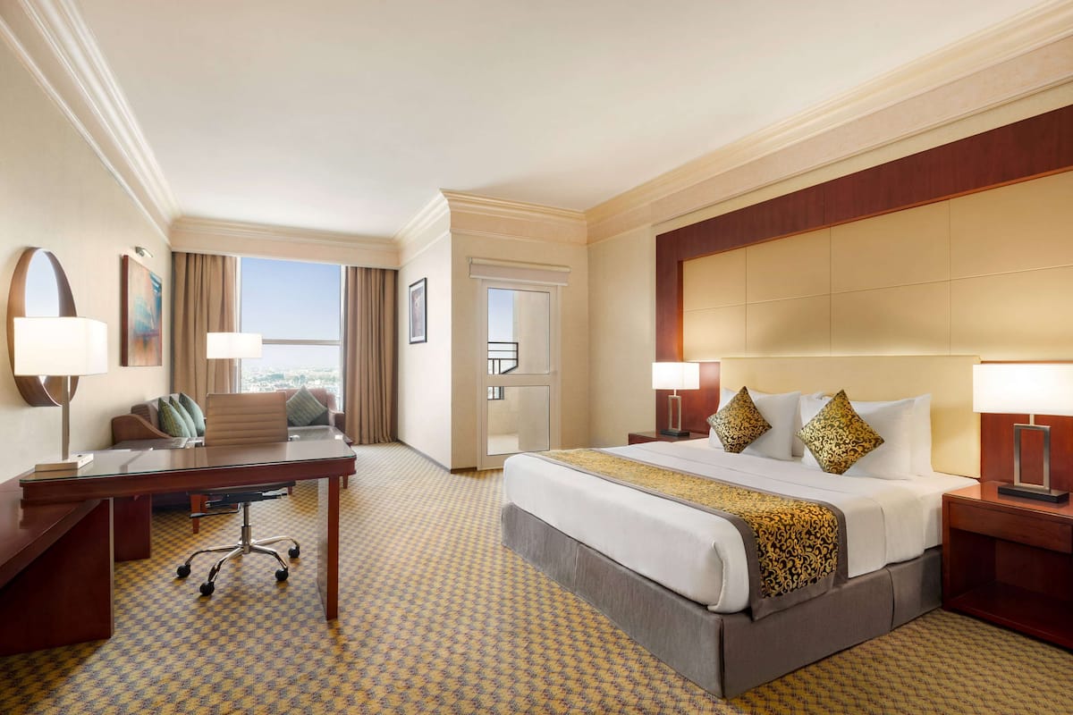 A hotel room with a large bed, a desk, a chair, and a view of the city.