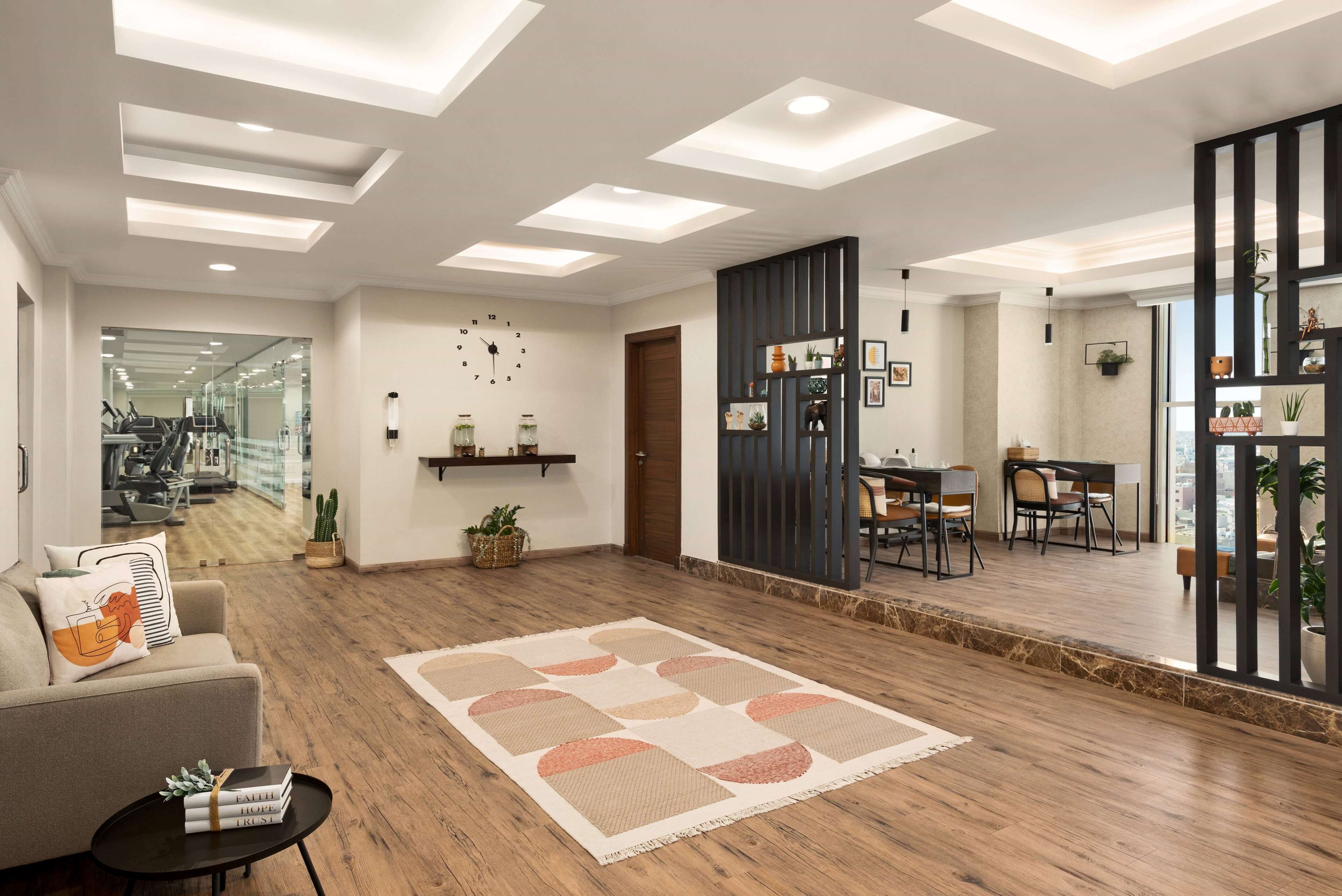 A modern living room with a wooden floor, a large rug, a sofa, a coffee table, and a dining area with chairs and a table.