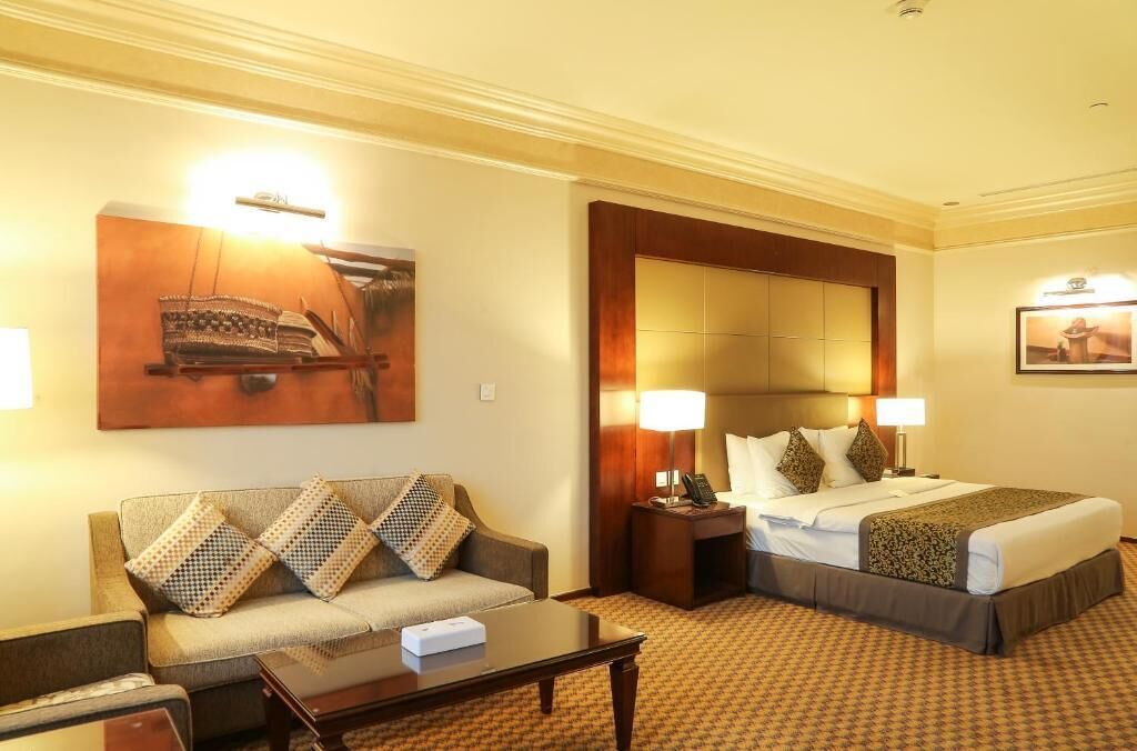 Una habitación de hotel con sofá, cama, mesita de noche y lámpara.