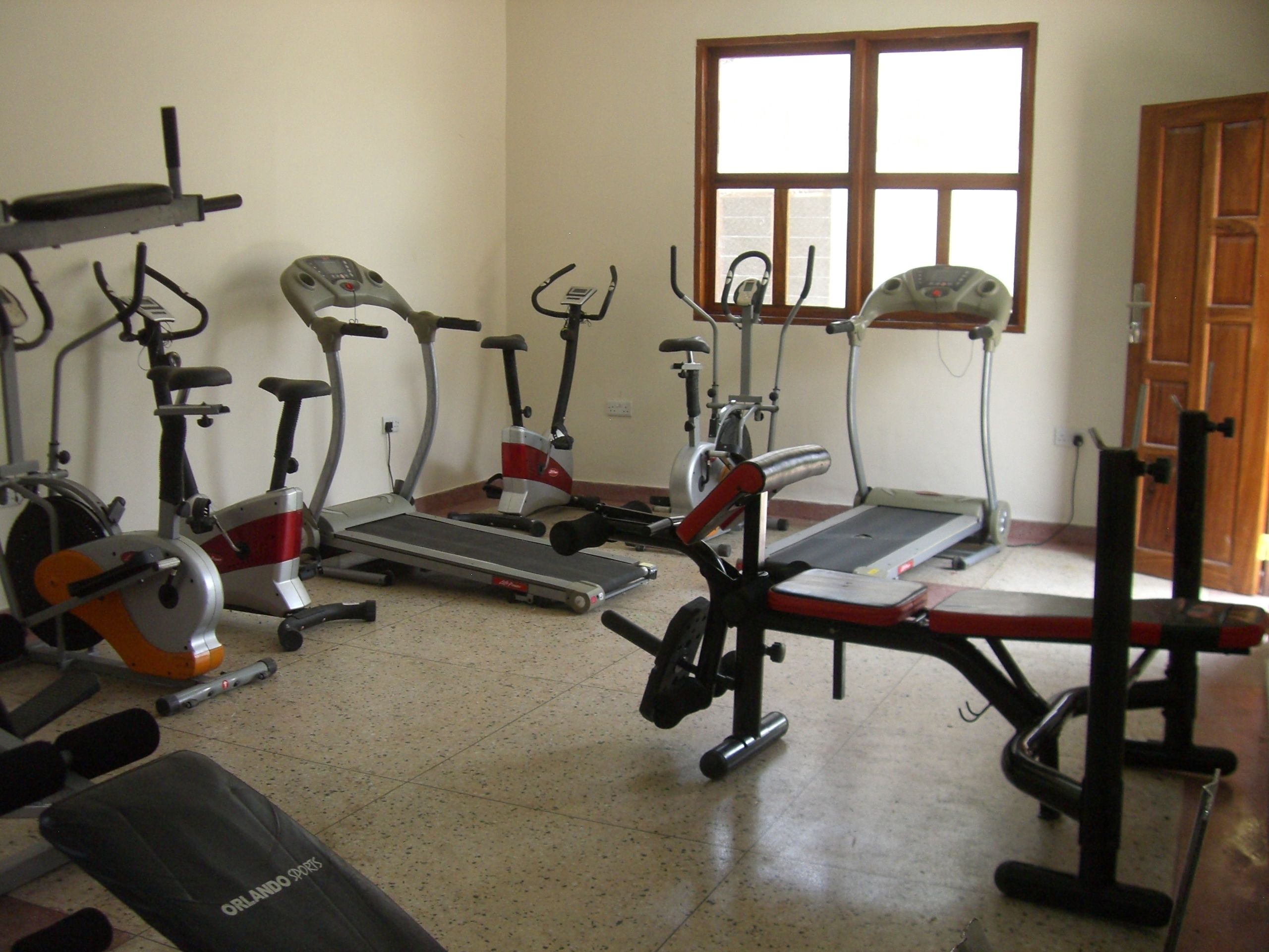 Un gimnasio en casa con varios equipos de ejercicio, incluyendo cintas de correr, bicicletas estáticas y una máquina de remo.