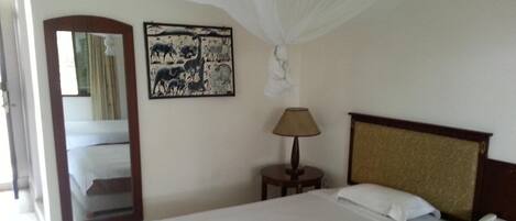 Una habitación de hotel con cama, lámpara de noche, teléfono, espejo y una obra de arte en la pared.