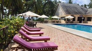 Ein Poolbereich mit Liegestühlen und Sonnenschirmen, ein Schwimmbecken und ein Gebäude mit Schildern für eine Bar und ein Restaurant.
