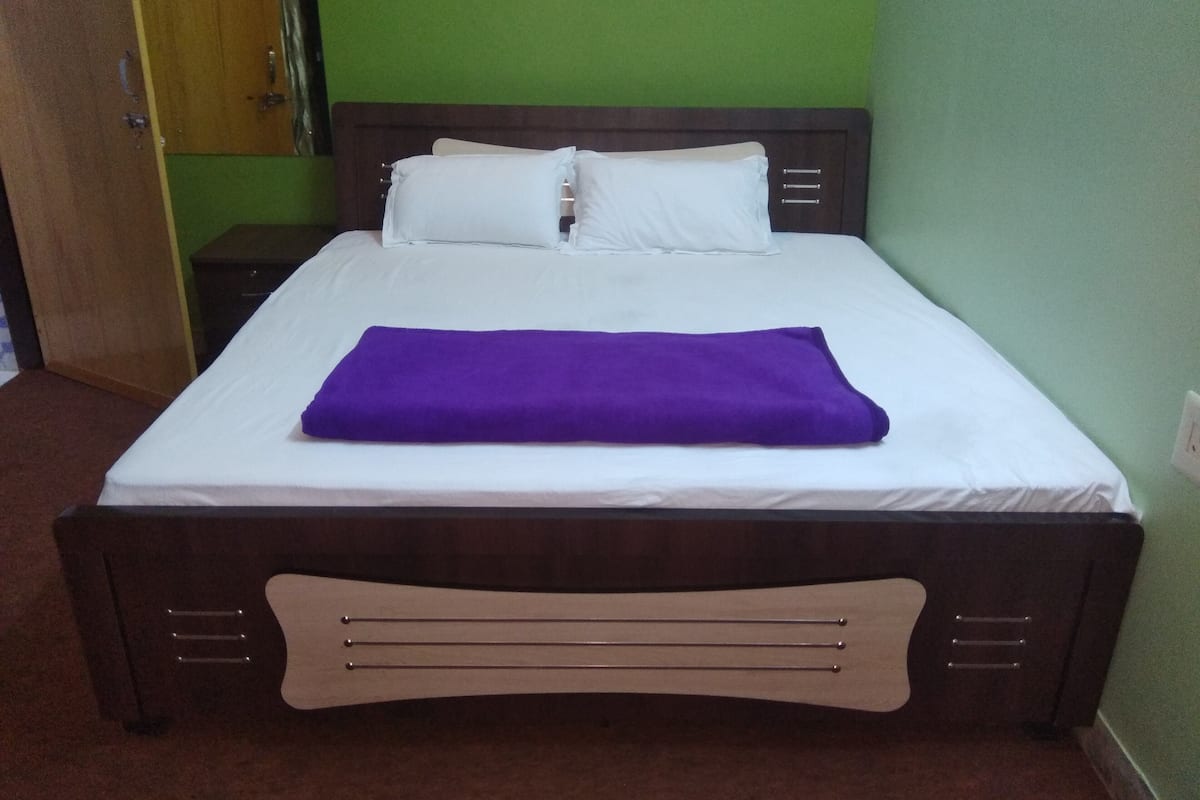 Een net opgemaakt bed met witte lakens en een paarse deken, een houten hoofdbord en een groene muur.