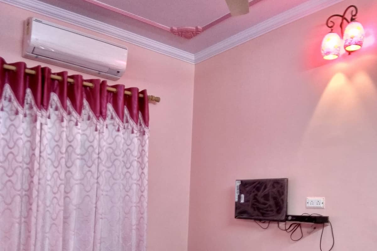Een kamer met een bed, een airconditioningapparaat, een wandplank met een stopcontact en een plafondventilator.