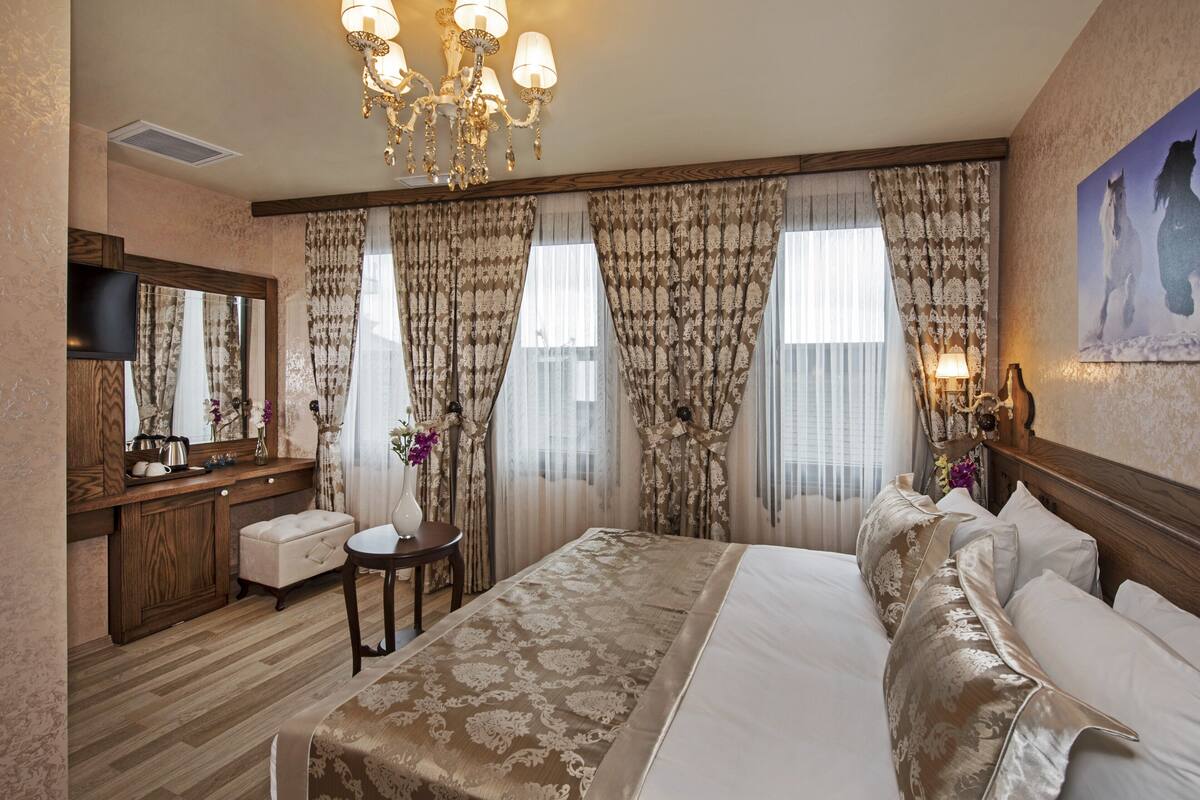 A hotel room with a large bed, a wooden dresser, a vanity, a television, and a chandelier.