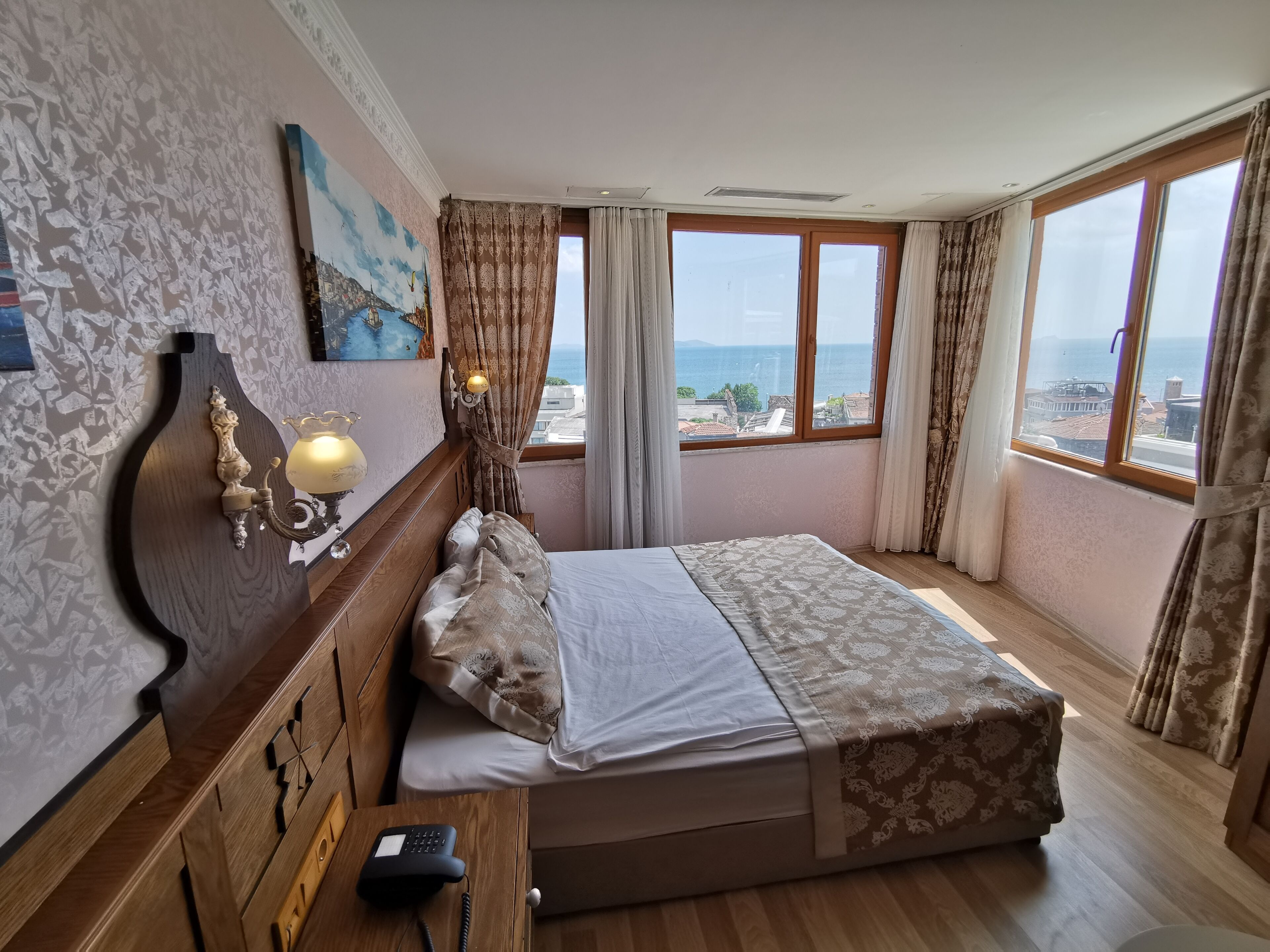 A hotel room with a bed, a telephone, a wall-mounted lamp, and a painting.