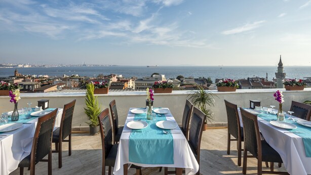 A rooftop dining area with tables set for four, overlooking a cityscape and the sea. - Perapolis Hotel (Istanbul)