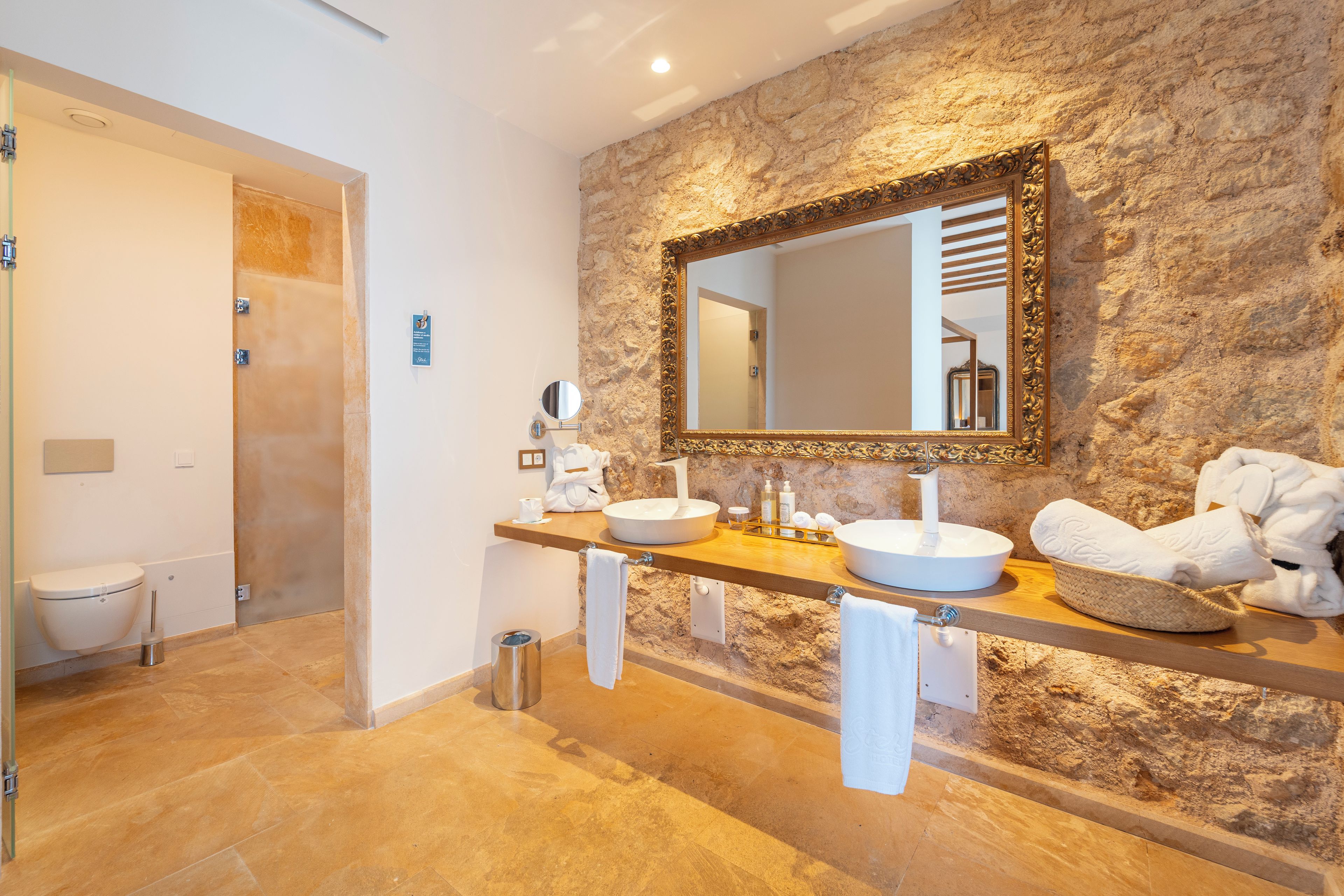 A bathroom with a stone wall, a large mirror, two sinks, and towels.