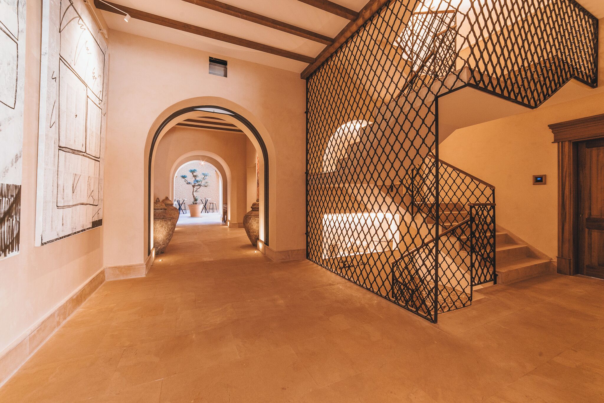 A hallway with a staircase, a large potted plant, and a view into another room.