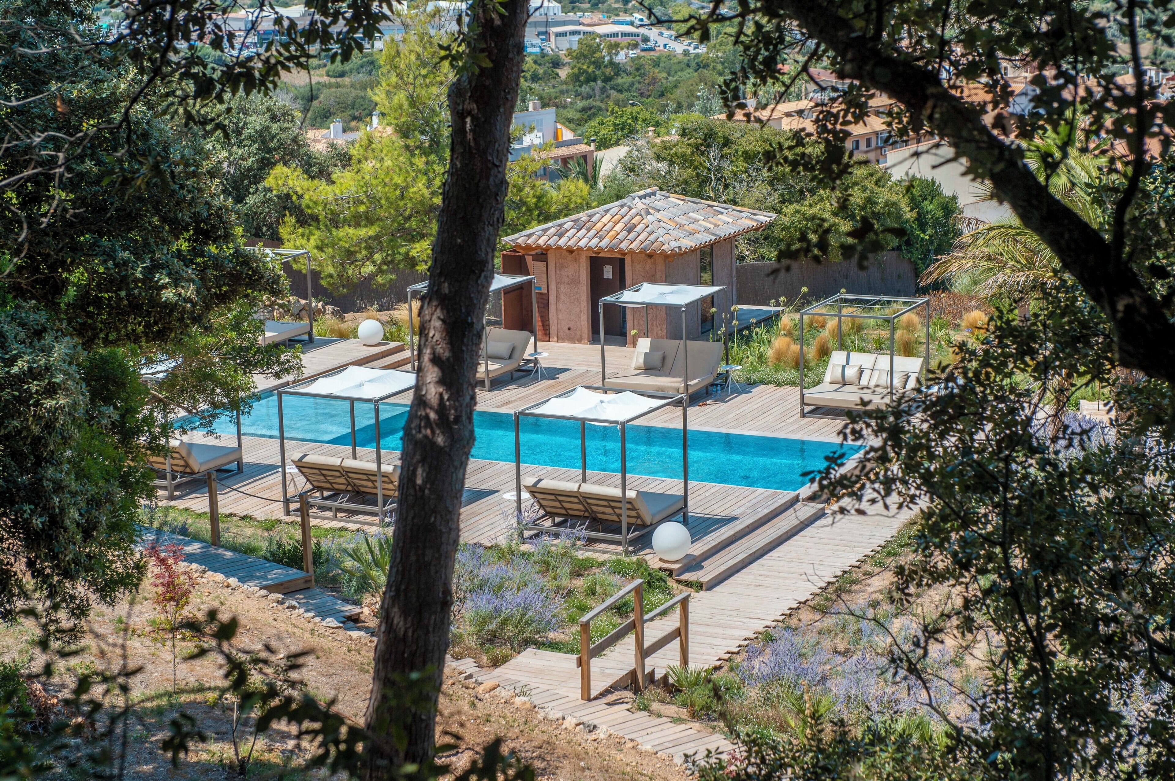 Zona de piscina con sillas de descanso y un pequeño edificio, rodeada de árboles y vegetación.