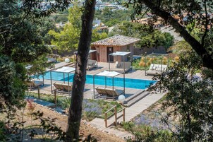 Zona de piscina con sillas de descanso y un pequeño edificio, rodeada de árboles y vegetación.