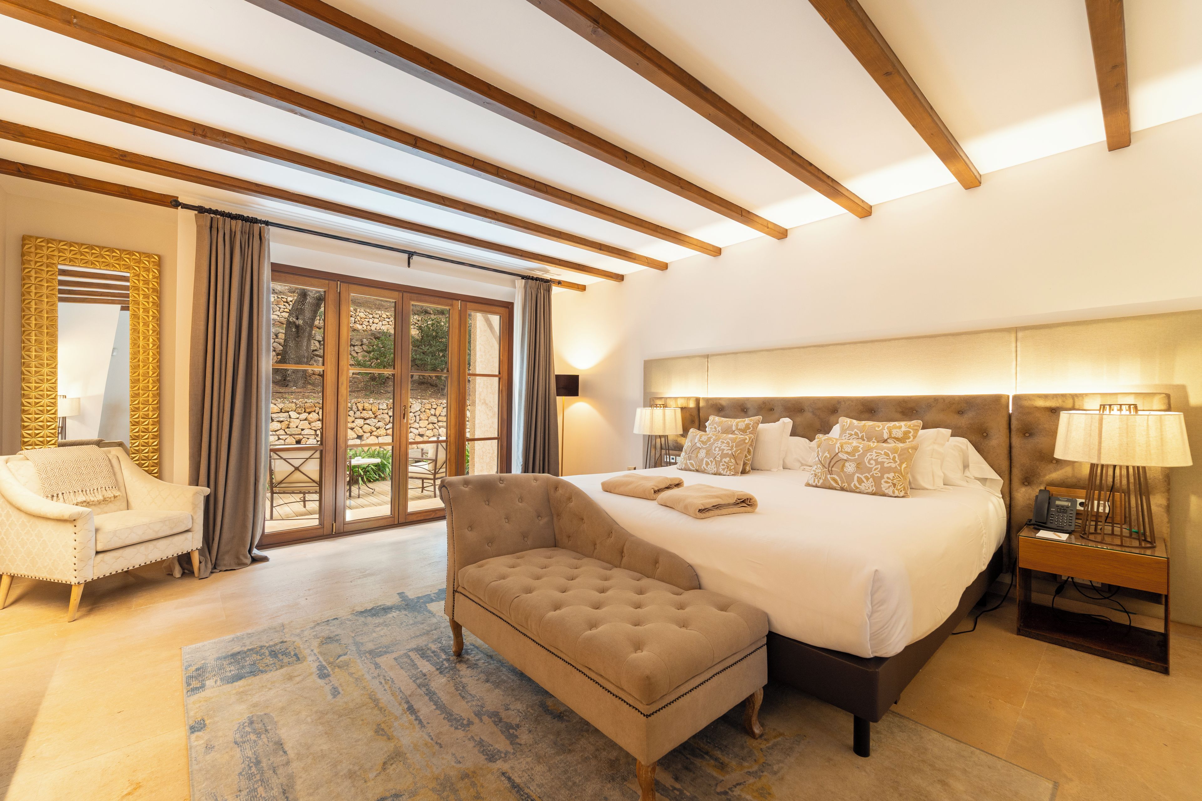 A spacious bedroom with a large bed, a sitting area, and a view through a glass door.