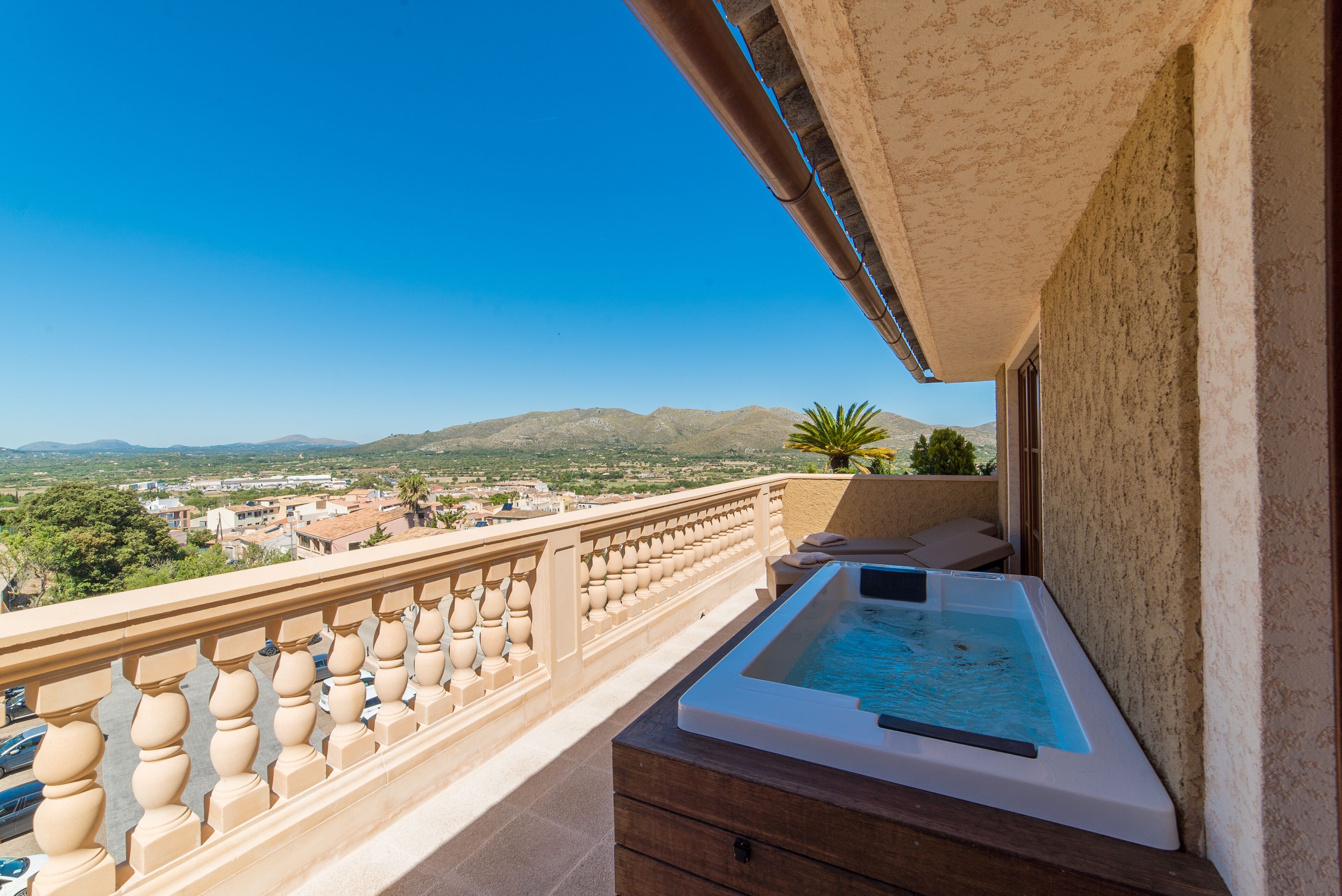 A balcony with a hot tub, a view of the countryside, and a mountain range in the background.