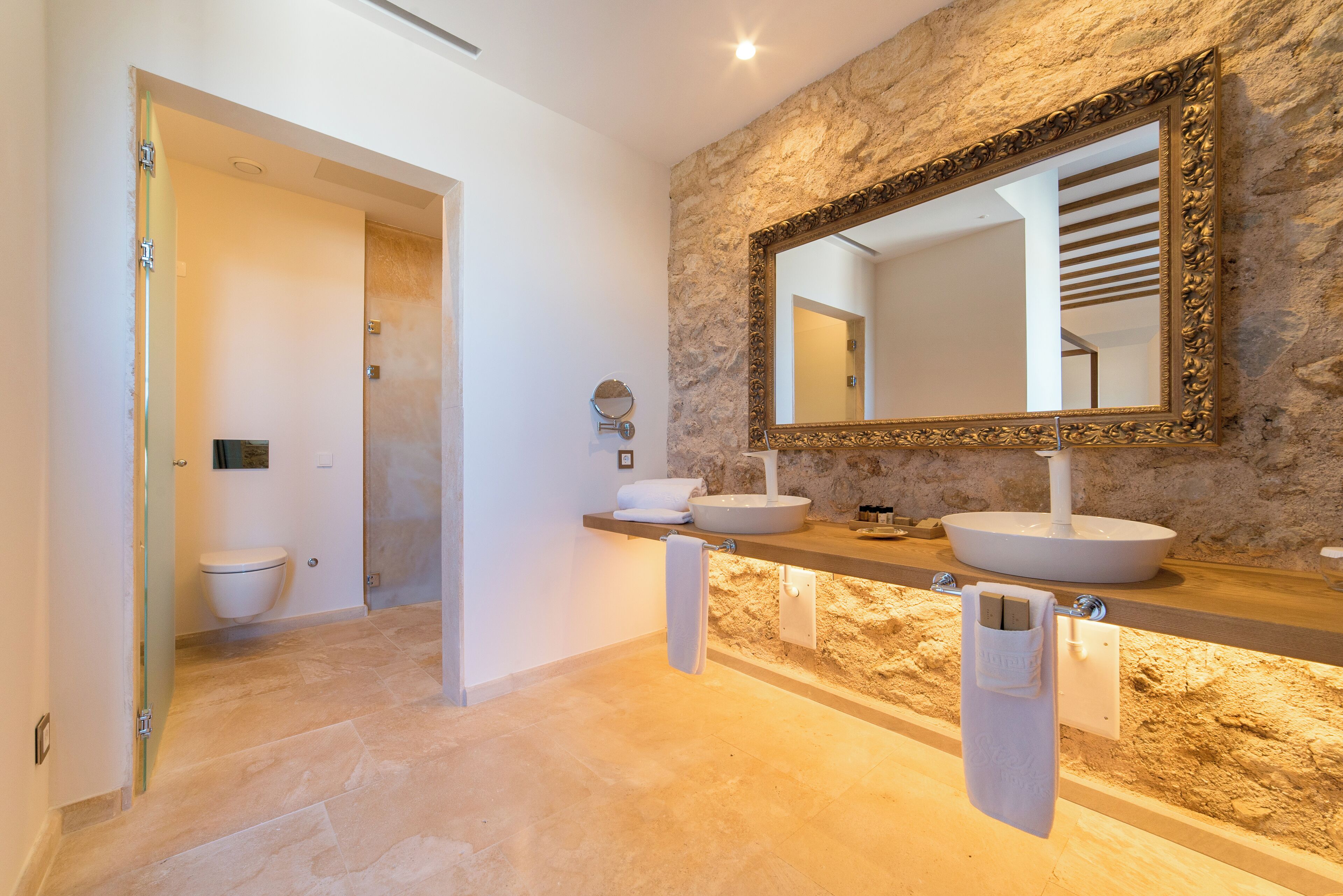 A bathroom with two sinks, a large mirror, and a stone wall.