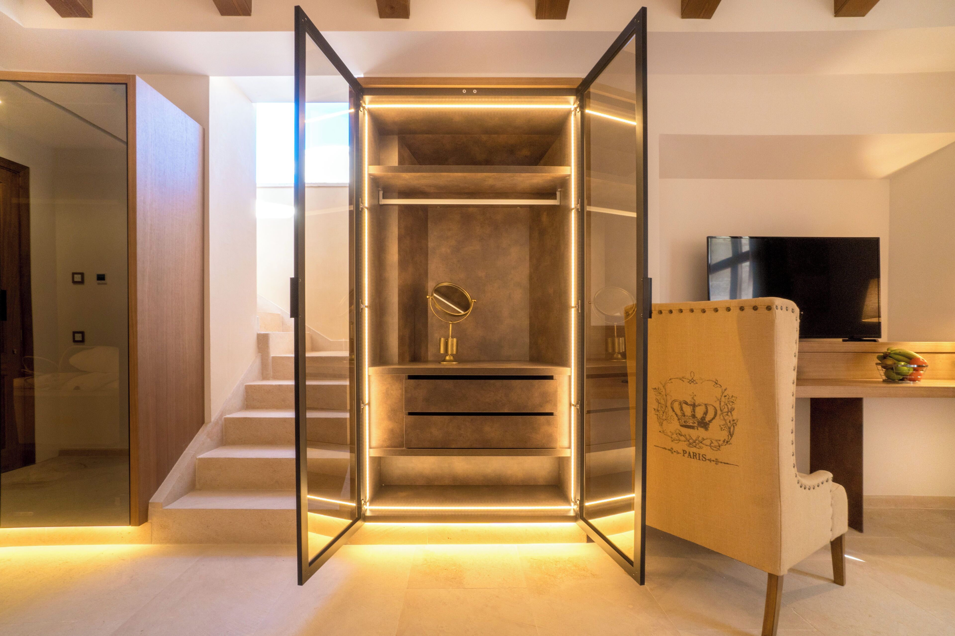 Un intérieur moderne avec un ascenseur à parois de verre, un escalier en bois et un coin salon équipé d’un téléviseur et d’un présentoir à fruits.