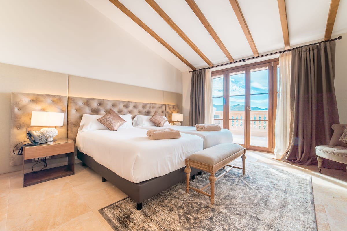 Um quarto espaçoso com uma cama grande, uma cama menor, um banco, uma mesa de cabeceira e vista para o exterior.