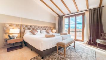 A spacious bedroom with a large bed, two bedside tables, a bench, and a view of the outdoors through a large window.