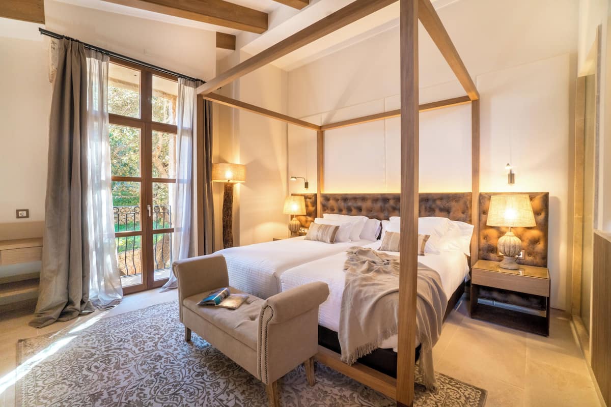 Uma cama com dossel e cortina, duas mesas de cabeceira, uma cadeira e vista para o exterior.