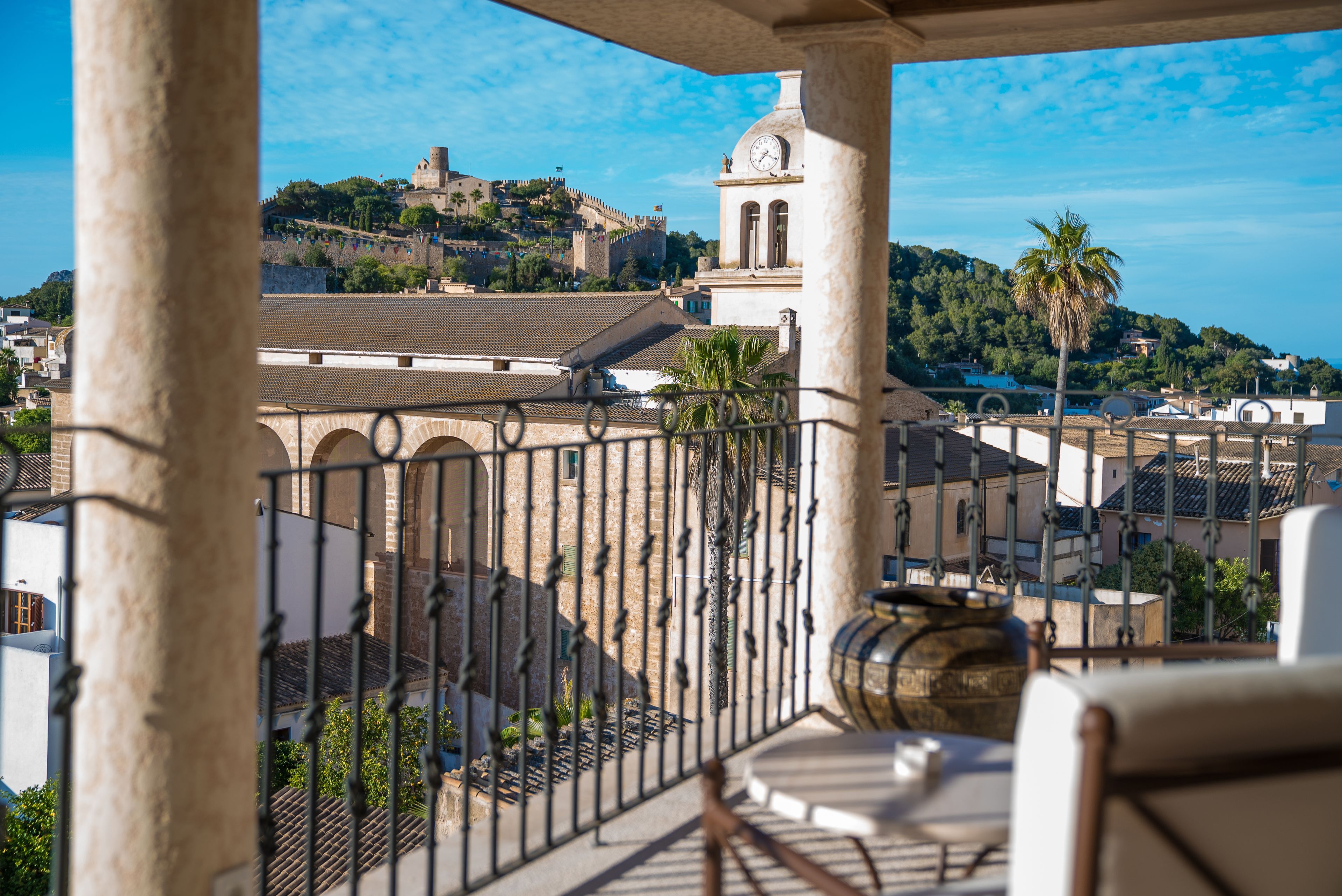 A balcony with a view of a historic town, including a prominent tower and a hill with buildings.