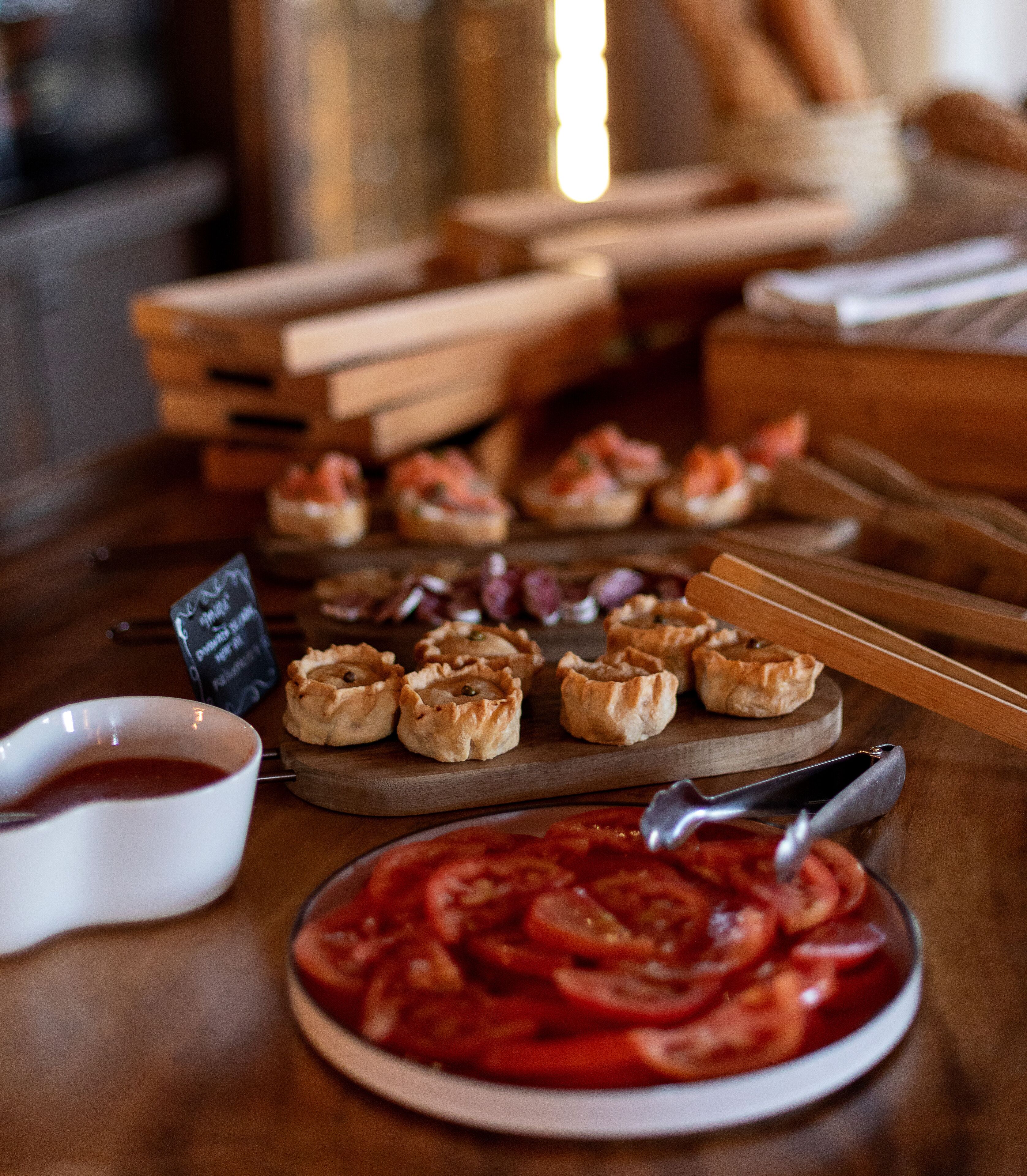 Una mesa de madera con comida, incluyendo un plato de tomates en rodajas y pequeños pasteles.