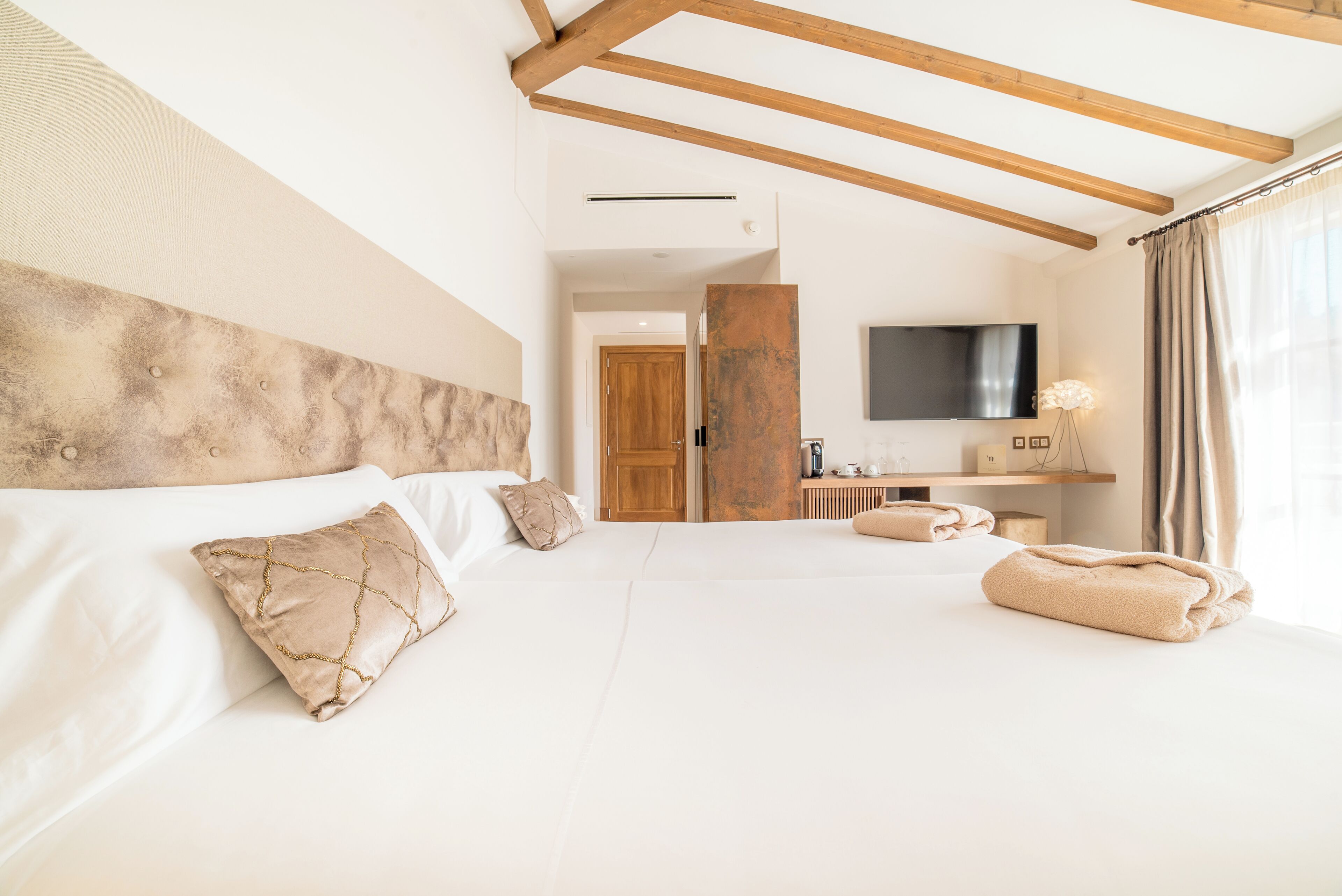 A hotel room with a large bed, wooden beams, a flat-screen TV, and a bathroom area.