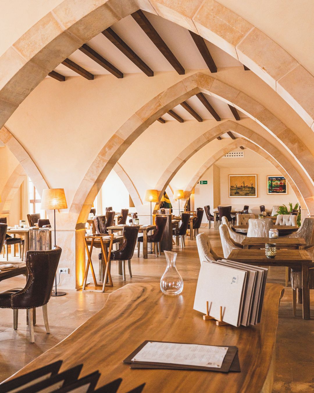 Un interior con techos abovedados, mesas y sillas de madera dispuestas para comer.