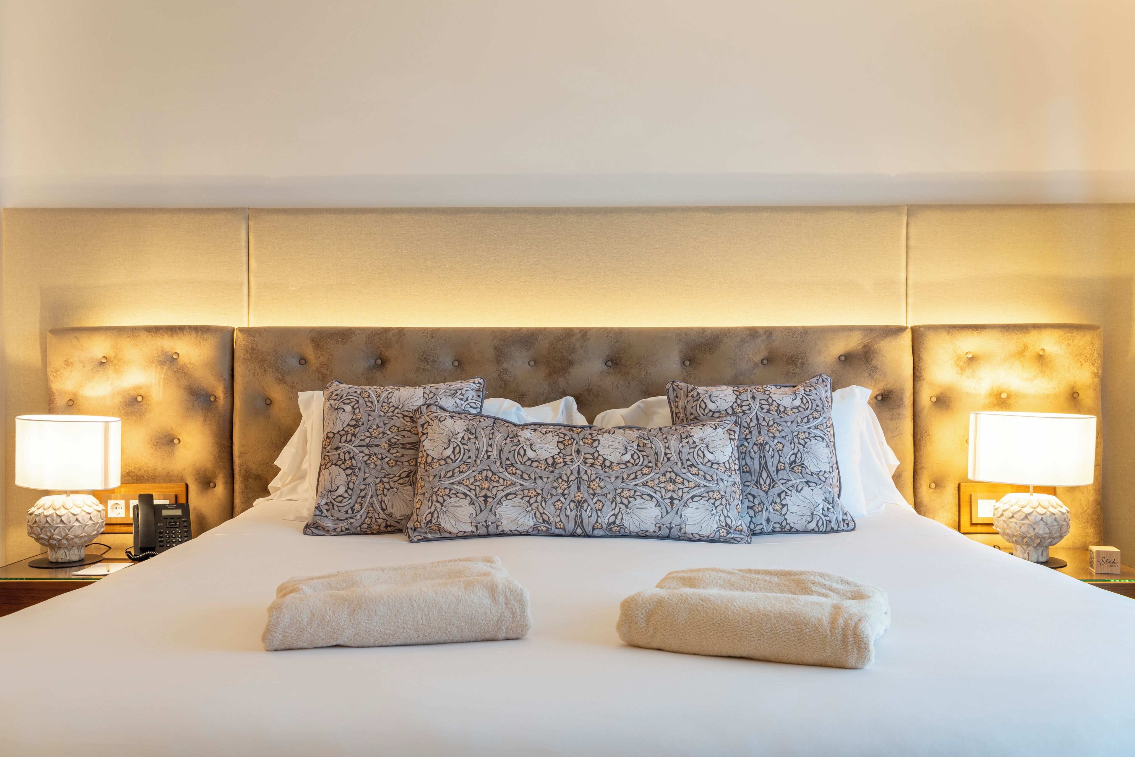 A hotel room with a large bed, two bedside lamps, and a headboard with tufting.