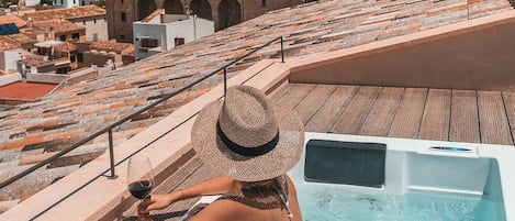 A person in a swimming pool on a deck with a view of a cityscape and a hill with buildings.