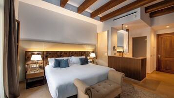 Una habitación de hotel moderna con una cama grande, lámparas de noche, un cabecero de madera, un sofá, un espejo y un mostrador de recepción de madera.