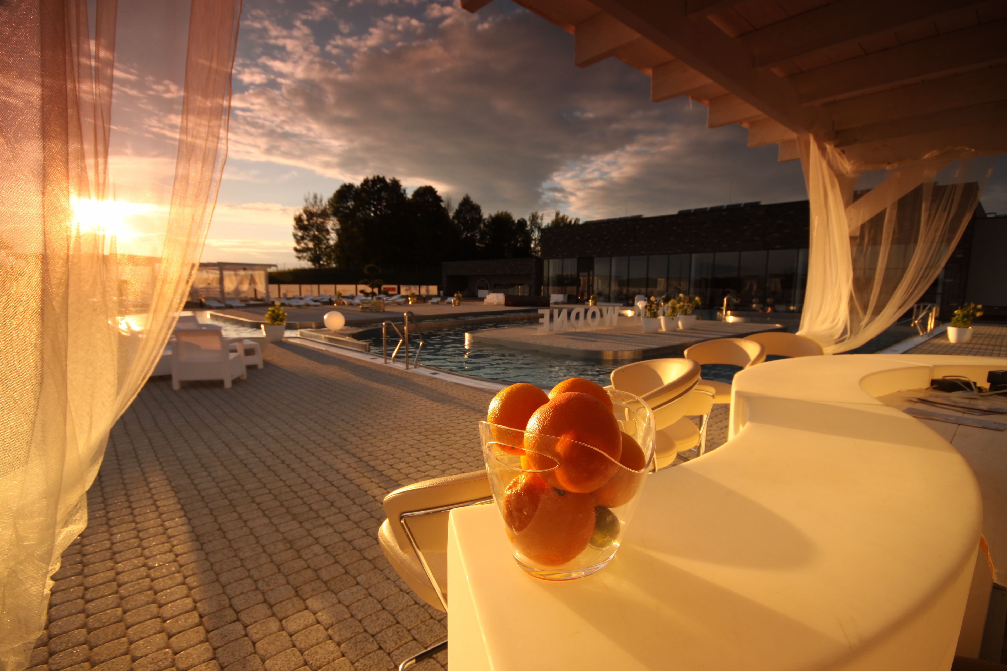 Una terraza con piscina, sillas de descanso blancas y una mesa de vidrio con naranjas.