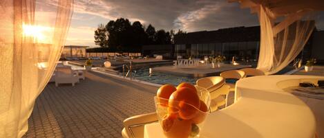 Una terraza con piscina, sillas de descanso blancas y una mesa de vidrio con naranjas.