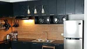 A modern kitchen with dark cabinetry, a stainless steel refrigerator, a wooden dining table with chairs, and pendant lights. - City Center Sleek Studio Deluxe (Bacolod)