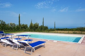 Una piscina con comode poltrone blu e vista sull'oceano.