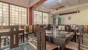 A restaurant with a high ceiling, large windows, and a ceiling fan. Tables and chairs are arranged for dining. - Itsy Hotels Paradise Inn, Haridwar (Haridwar)