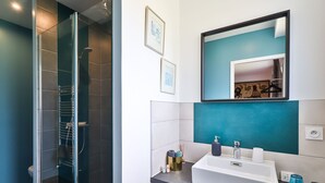 A modern bathroom with a glass shower enclosure, a white sink with a blue countertop, and a mirror with a teal accent wall. - Chambre d'Hôtes Txori Etxea (Arcangues)