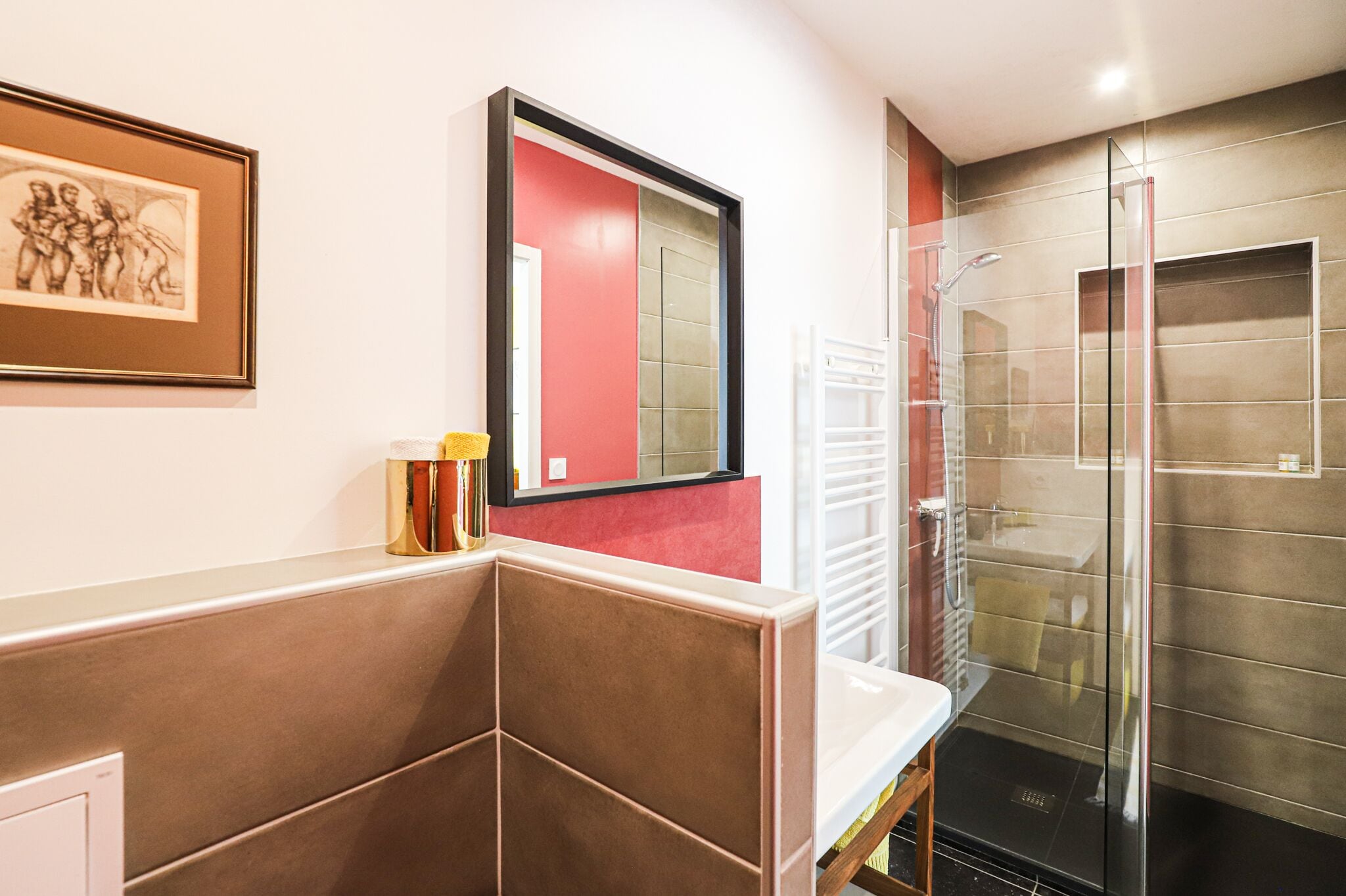 A modern bathroom with a glass shower enclosure, a white sink, and a framed artwork on the wall.