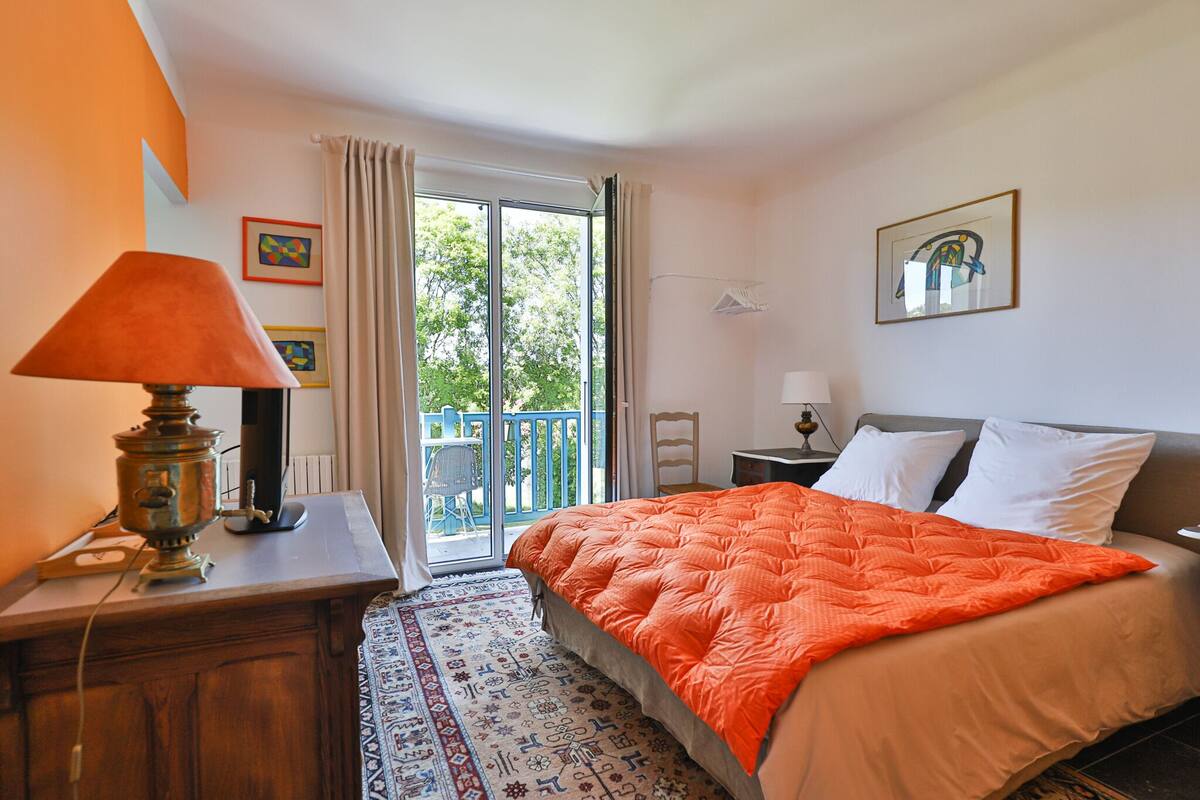 Ein Schlafzimmer mit Bett, Nachttisch, Lampe, Heizkörper und Blick ins Freie.