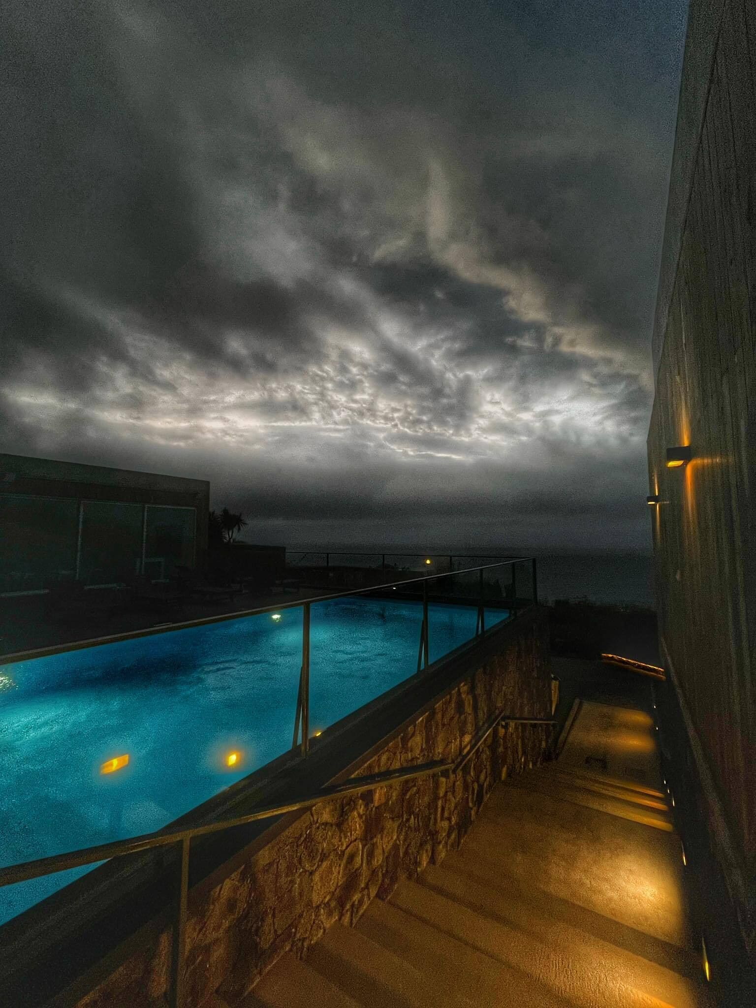Zwembadgedeelte met een stenen muur en hekwerk, onder een bewolkte lucht.
