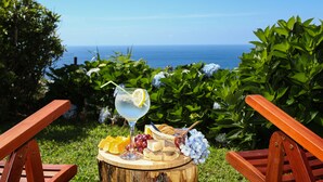 A picnic setup with a glass of lemonade, fruits, cheese, and bread on a wooden table, overlooking a scenic ocean view.
