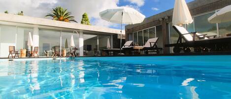 A swimming pool with lounge chairs and umbrellas, surrounded by modern architecture.
