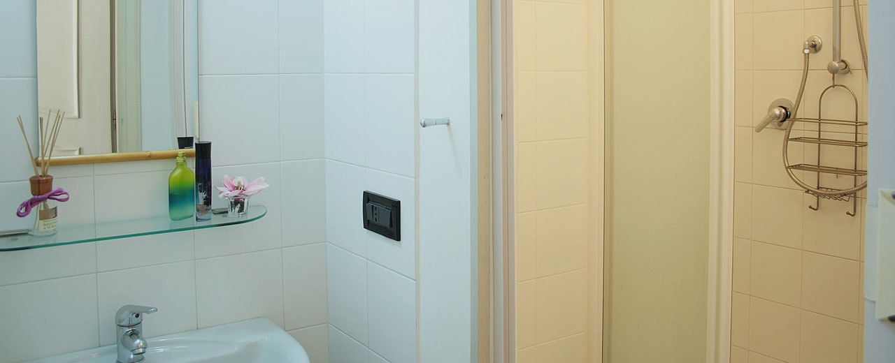 Ein Badezimmer mit einer Glasablage für Toilettenartikel, einer Dusche mit Ablagegestell und einer an der Wand montierten Bedienkonsole.