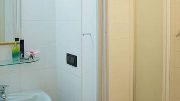 Ein Badezimmer mit einer Glasablage für Toilettenartikel, einer Dusche mit Ablagegestell und einer an der Wand montierten Bedienkonsole.