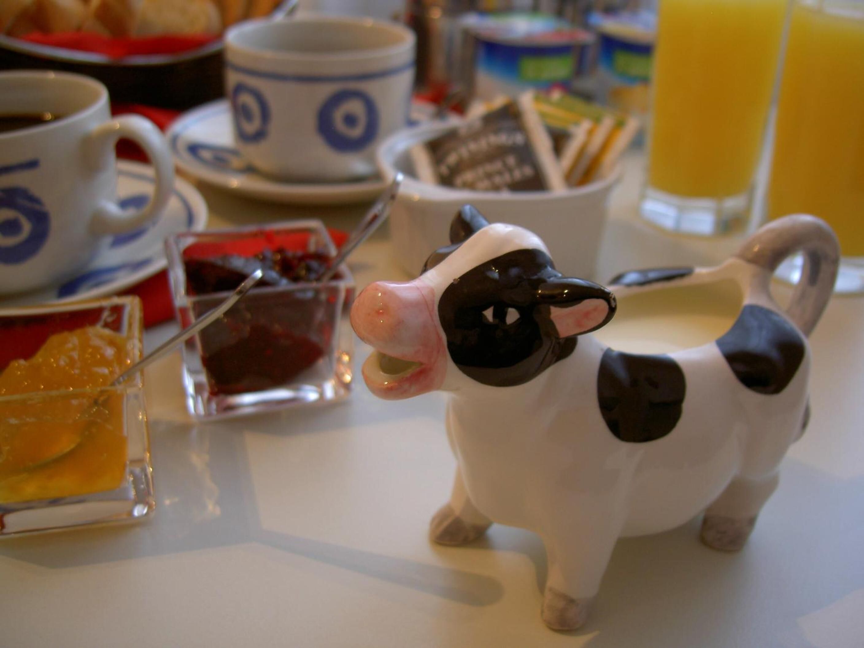 Une table à manger ornée d’une figurine de vache en céramique, d’une tasse, d’un verre de jus d’orange et de divers aliments pour le petit-déjeuner.