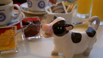 Une table à manger ornée d’une figurine de vache en céramique, d’une tasse, d’un verre de jus d’orange et de divers aliments pour le petit-déjeuner.
