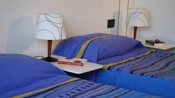 A hotel room with two beds, each with a blue bedspread and a matching pillow. There are two bedside tables, each with a lamp and a book.