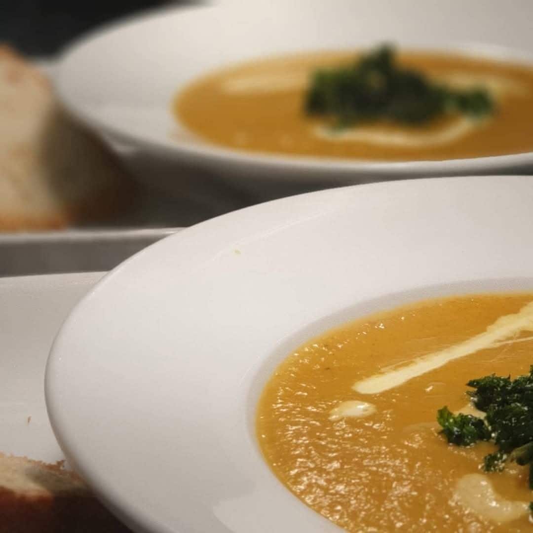Un tazón blanco de sopa con un adorno sobre una bandeja.