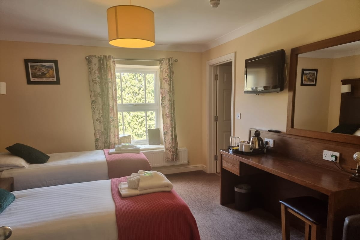 A hotel room with two beds, a wooden dresser, a television, and a window with curtains.