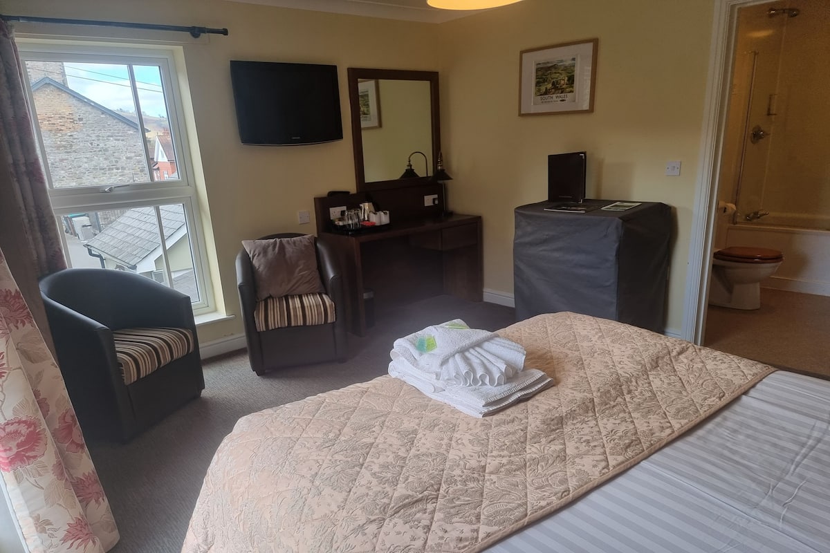 A hotel room with a bed, a desk, a chair, a television, and a bathroom visible through an open door.