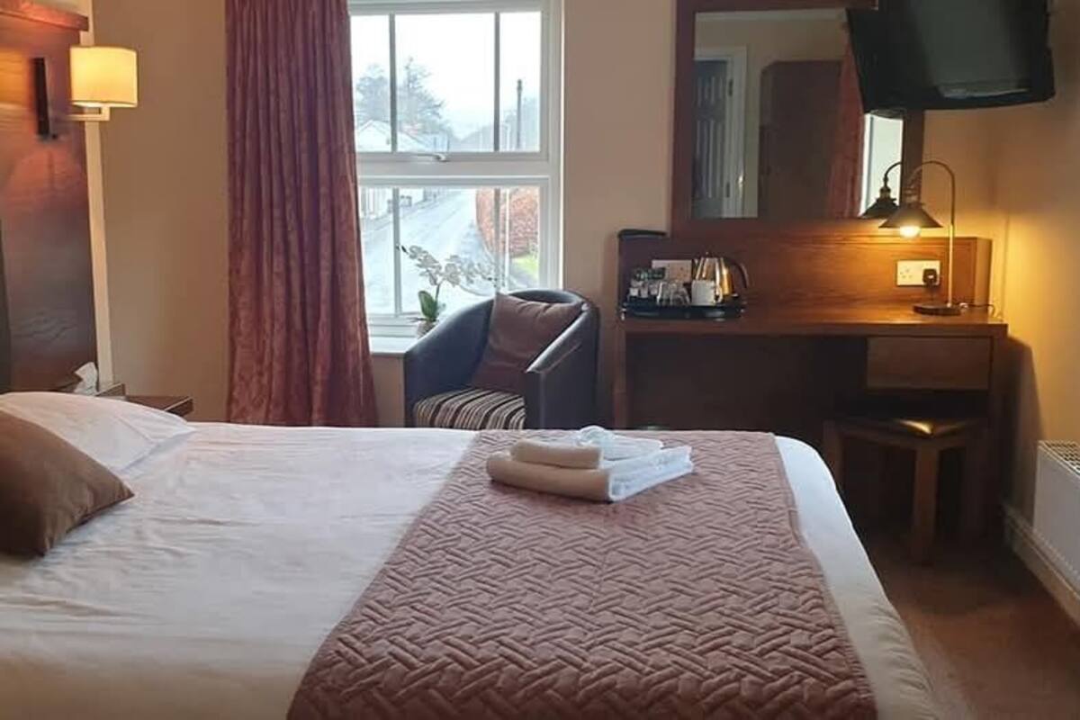 A hotel room with a large bed, a desk, a chair, and a TV.